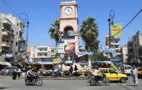 People ride on their motorbikes along a street at the clock square in the city of Idlib