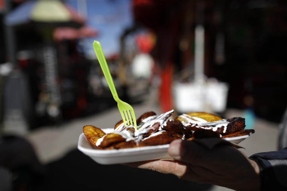 A customer receives his order of fried plantains, served on a non-biodegradable disposable plate along with a plastic fork, from a street vendor in central Mexico City, Friday, Jan. 1, 2021. The few street food vendors out working on New Year's Day amid the COVID-19 pandemic said they were either unaware of or were still figuring out how to comply with a broad ban on single-use containers, forks, straws, and other ubiquitous items that took effect Friday in Mexico's capital, one of the world's largest cities, after more than a year of preparation. (AP Photo/Rebecca Blackwell)