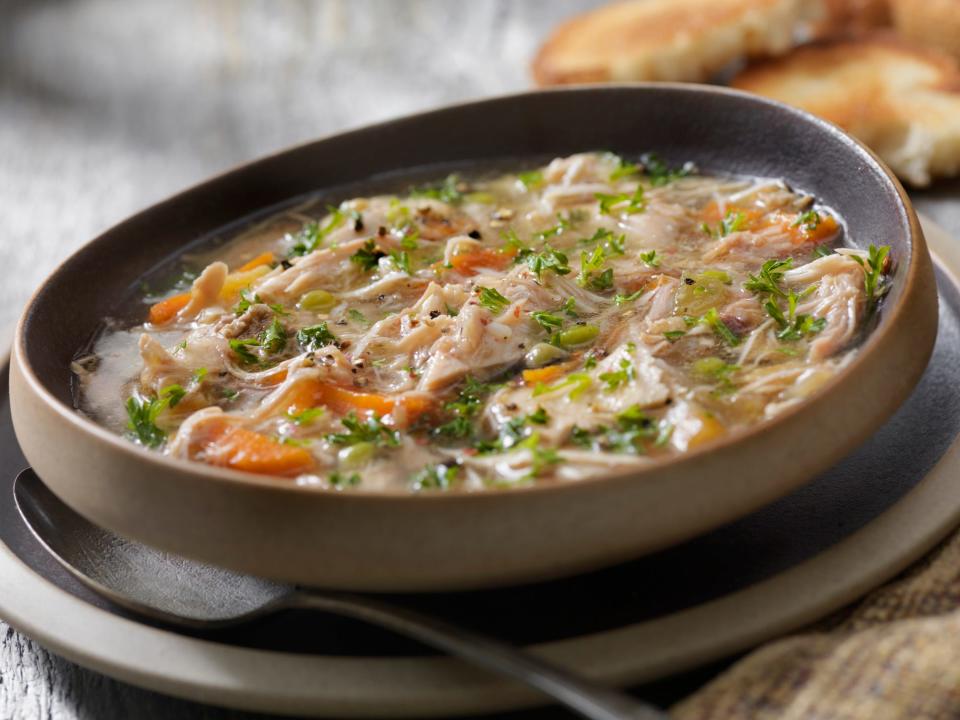 A close up of a bowl of turkey soup with herbs and carrots.
