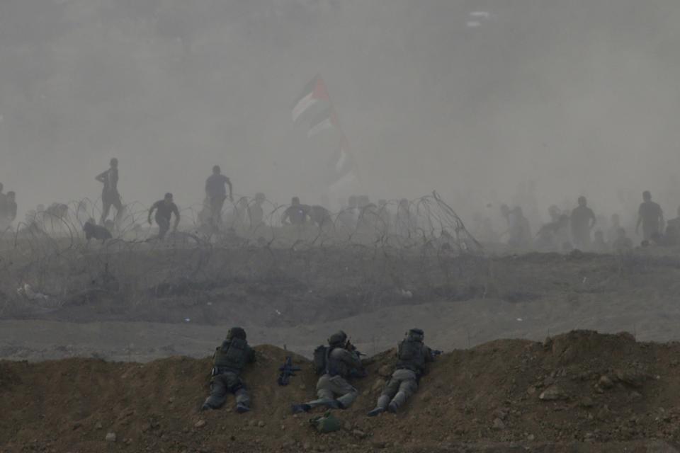 Israeli soldiers are positioned on a sand berm as Palestinian protesters run from tear gas fired by Israeli troops during a protest along the Israel Gaza border, Israel, Friday, Oct. 19, 2018. (AP Photo/Ariel Schalit)