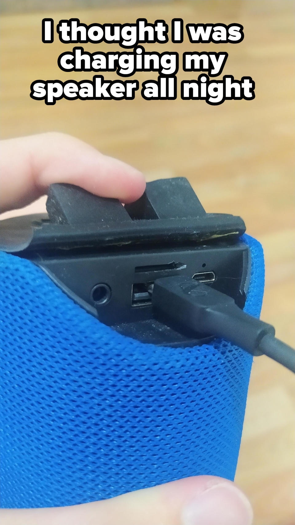 A hand is plugging a USB cable into a blue portable speaker