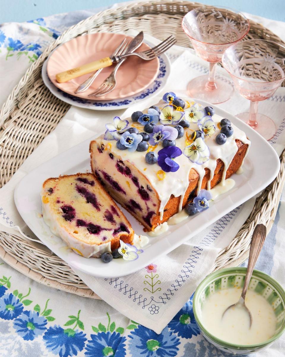 blueberry lemon loaf with lemon glaze and fresh blueberries and pansies on top for garnish