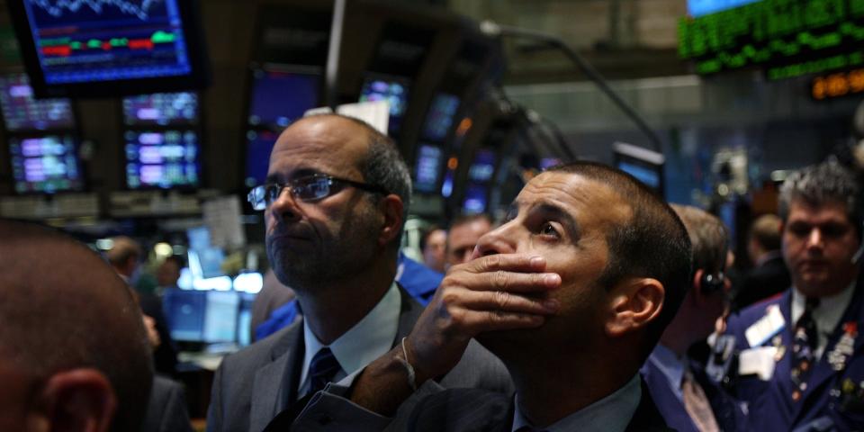 Traders looking up at stocks, one with his hand over his mouth.