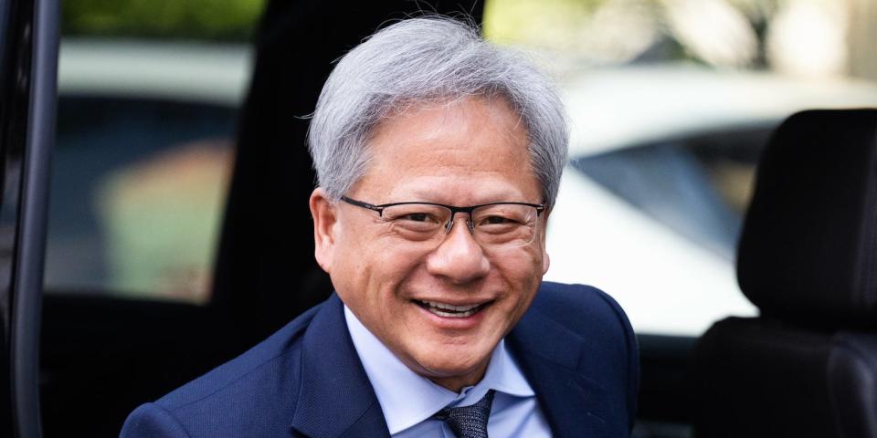 Jensen Huang smiling whilst wearing a navy blue suit, light blue shirt and dark blue tie