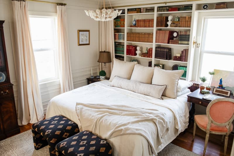 Books on shelf behind neatly made bed.