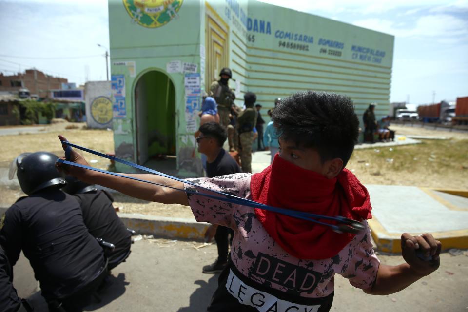 A young man joins forces with riot police as he uses his sling shot against supporters of ex-President Pedro Castillo protesting his detention, on the Pan-American North Highway, in Chao, Peru, Thursday, Dec. 15, 2022. Violent protests disrupting tourism and trade across Peru persisted Thursday as a judge considered whether to keep the country’s ex-president in custody while authorities build their case against him for inciting a rebellion. (AP Photo/Hugo Curotto)