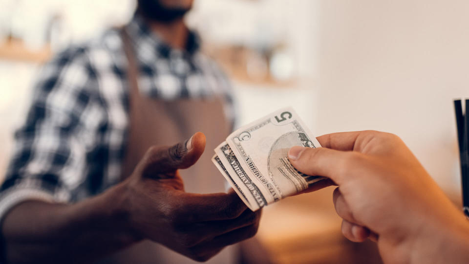 selective focus of african american barista taking cash payment on bar counter in cafe.