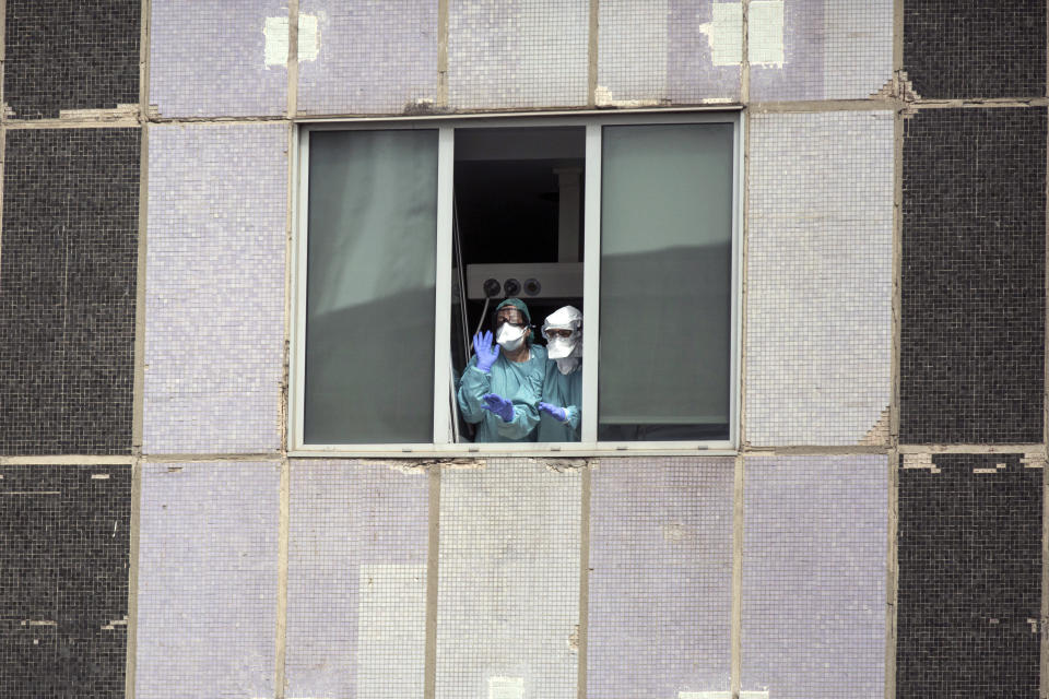 Medical workers wearing face masks gesture from hospital La Paz in Madrid, Spain, Wednesday, March 18, 2020. Spain will mobilize 200 billion euros or the equivalent to one fifth of the country's annual output in loans, credit guarantees and subsidies for workers and vulnerable citizens, Prime Minister Pedro Sanchez announced Tuesday. For most people, the new coronavirus causes only mild or moderate symptoms. For some, it can cause more severe illness, especially in older adults and people with existing health problems. (AP Photo/Manu Fernandez)