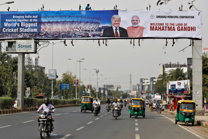 A worker installs a hoarding with the images of the US President Donald Trump and India's Prime Minister Narendra Modi, as commuters move past, ahead of Trump's visit, in Ahmedabad