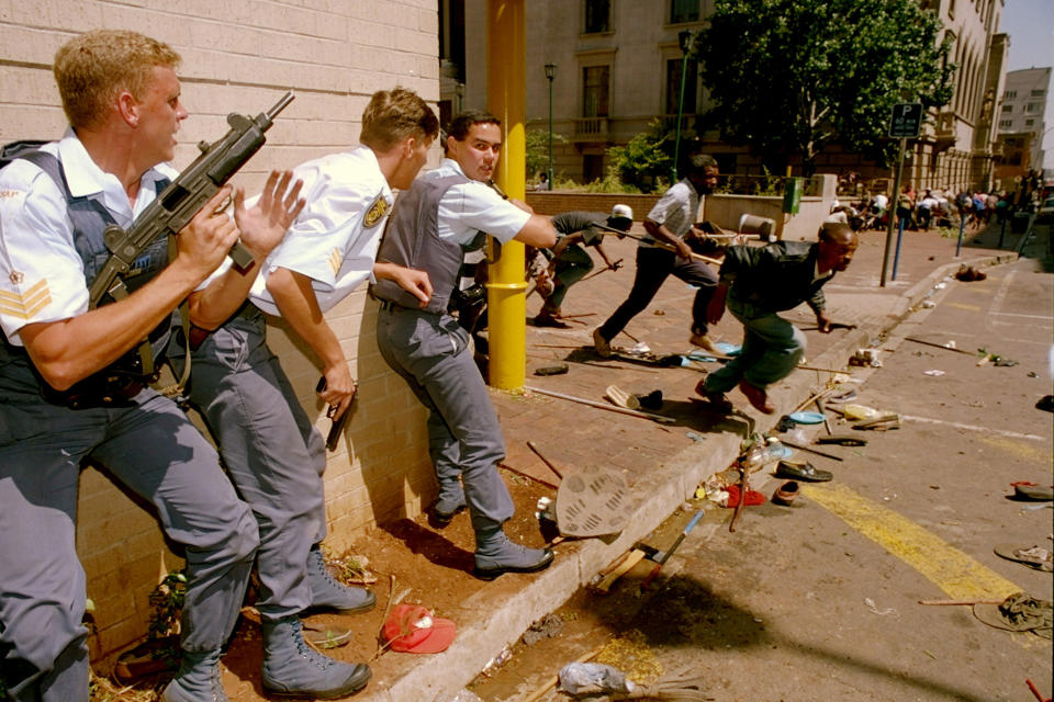 FILE - Police take cover as Zulu Inkatha Freedom Party (IFP) supporters flee as they are fired upon by unidentified gunmen, March 28, 1994, in Johannesburg. South Africa is engrossed in debate over the legacy of apartheid's last president, F.W. de Klerk, who died at 85 and is to be buried Sunday, Nov 21, 2021. Some people want to remember de Klerk as the liberator of Nelson Mandela, but others say he was responsible for racist murders. (AP Photo/Peter Dejong, File)