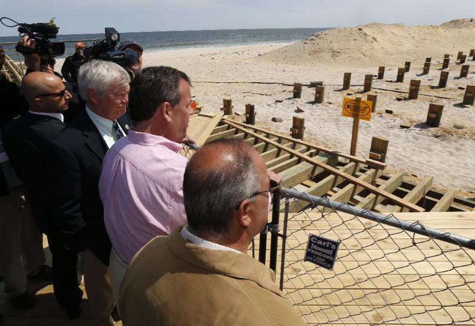 New Jersey Gov. Chris Christie, center right, stands behind a fence with Seaside Park Mayor Robert Matthies, second from left, and Seaside Heights Mayor William Akers, right, while looking at reconstruction of the Seaside Park boardwalk, Friday, April 25, 2014, in Seaside Heights, N.J. Christie visited the boardwalk to see progress following last September's massive fire that burned down the Seaside Park side of the boardwalk. Previously, the boardwalk had been rebuilt following Superstorm Sandy. Investigators determined the fire started in wiring under the boardwalk in Seaside Park that had been damaged by exposure to storm water from Sandy. (AP Photo/Julio Cortez)