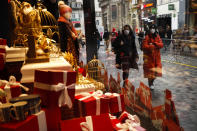 People, wearing face masks to prevent the spread of the coronavirus, walk past a display windows of a shopping mall in a commercial street in downtown Brussels, Tuesday, Dec. 1, 2020. Non-essential shops in Belgium are reopening on Tuesday in the wake of encouraging figures about declining infection rates and hospital admissions because of the coronavirus. (AP Photo/Francisco Seco)