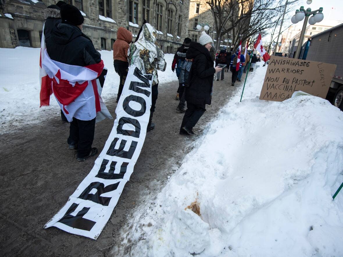 A person drags a banner as they walk towards Parliament Hill for a rally against COVID-19 restrictions, which began as a cross-country convoy protesting a federal vaccine mandate for truckers in Ottawa on Saturday. (Justin Tang/Canadian Press - image credit)