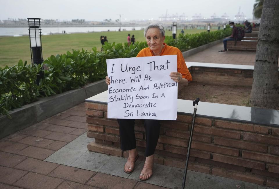 Prof. Kumari Jayawardena, a leading Sri Lankan academic and feminism activist holds a placard demanding political and economic stability in the country near the ongoing protest site as the Chinese funded sea reclamation Port City project is seen in the background in Colombo, Sri Lanka, Monday, May 2, 2022. Sri Lanka is near bankruptcy and has announced it is suspending payments on its foreign loans until it negotiates a rescue plan with International Monetary Fund. (AP Photo/Eranga Jayawardena)