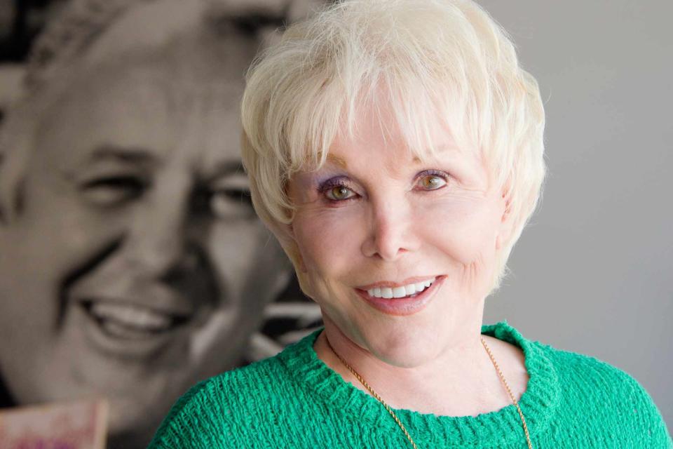 <p>Roxanne McCann/Getty</p> Joan Benedict Steiger poses in front of a photo of her late husband,  actor Rod Steiger in 2013 at her home in Malibu, California