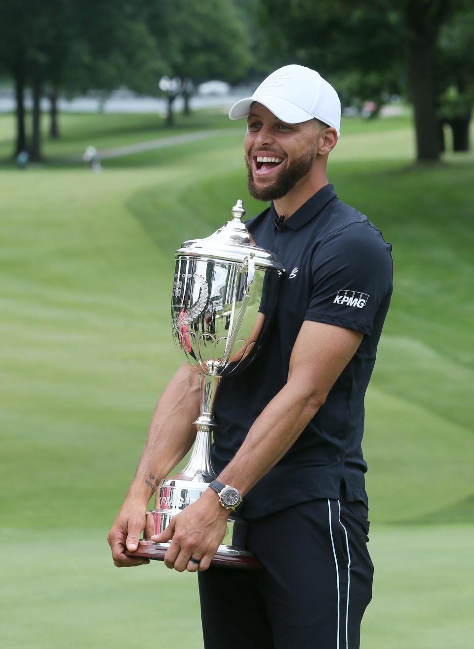 Stephen Curry holds the Underrated Golf tournament trophy as workers mover the trophy stand on the 18th green on the South Course at Firestone Country Club in Akron.