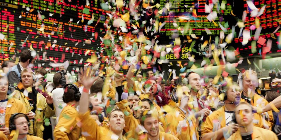 Traders celebrating, dressed in yellow and throwing confetti.