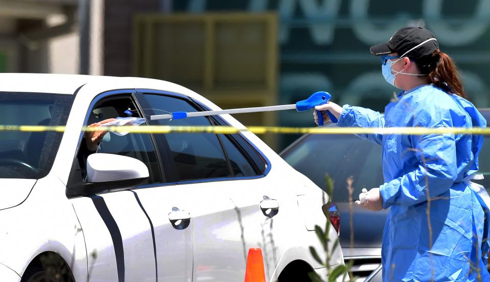 A healthcare volunteer in protective gear grabs a novel coronavirus, COVID-19, test kit from a driver with a tong at a mobile test site in Los Angeles, Caifornia on May 6, 2020. - Some retailers in California, including bookstores, flower shops and clothing stores, will be allowed to reopen for business at the end of the week, the state's governor announced on Monday. (Photo by Frederic J. BROWN / AFP) (Photo by FREDERIC J. BROWN/AFP via Getty Images)