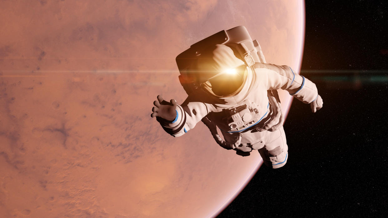  An astronaut floating in space in front of a large reddish planet 