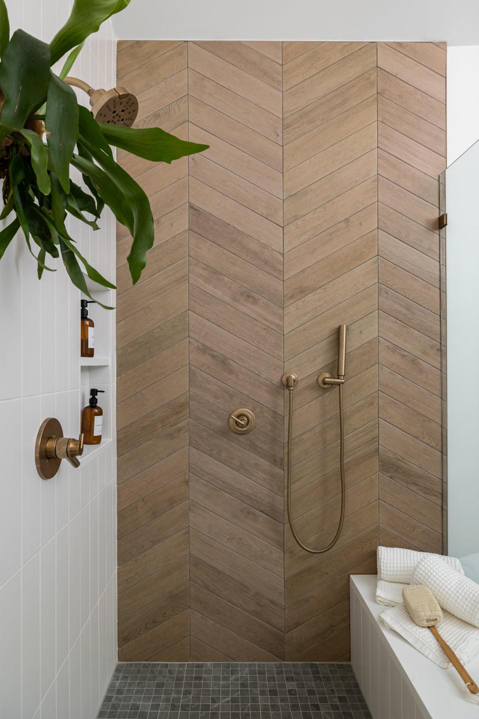 A faux wood tile wall in a chevron lay pattern brings neutral tones into the shower in this renovated home.