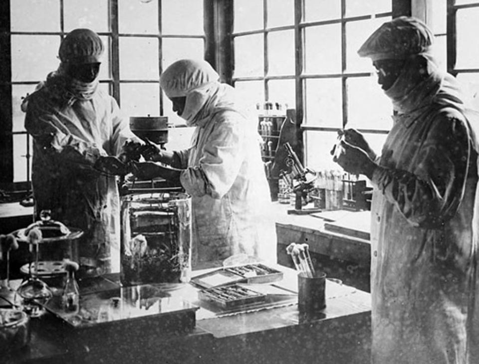 Three unidentified individuals in protective gear work in a laboratory setting