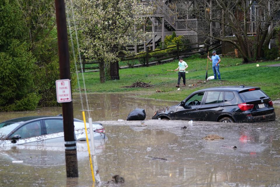 Residents observe cars flooded in a low-lying parking lot and grassy area, Tuesday, April 2, 2024, near the intersection of Delta Avenue and Columbia Parkway in the Columbia Tusculum neighborhood in Cincinnati. Several homes that sit at the base of a hill near the intersection have flooded, neighbors said.