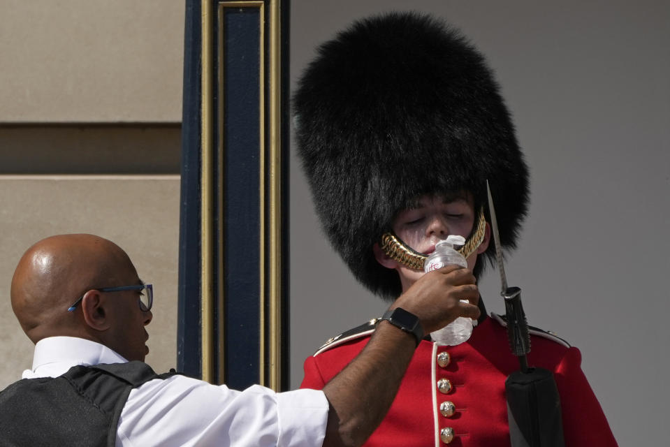 A police officer givers water to a British soldier wearing a traditional bearskin hat, on guard duty outside Buckingham Palace, during hot weather in London, Monday, July 18, 2022. The British government have issued their first-ever "red" warning for extreme heat. The alert covers large parts of England on Monday and Tuesday, when temperatures may reach 40 degrees Celsius (104 Fahrenheit) for the first time, posing a risk of serious illness and even death among healthy people, the U.K. Met Office, the country's weather service, said Friday. (AP Photo/Matt Dunham)