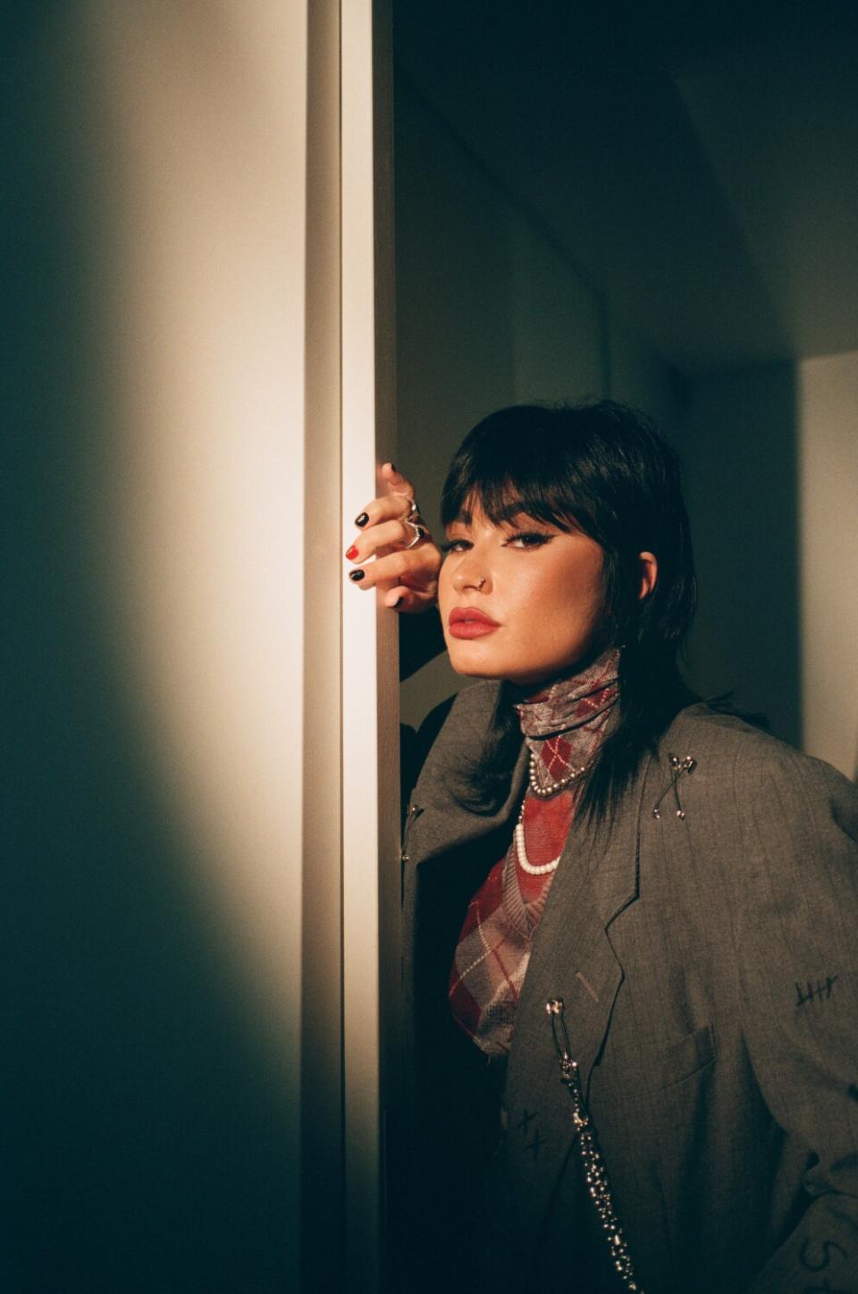 A woman with a shag haircut leans against a door frame.