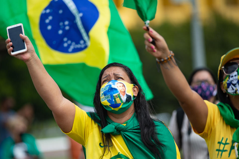 BRASILIA, BRAZIL - MAY 24: Supporters of Brazilian President Jair Bolsonaro wearing face masks with his face wave and shout slogans during a demonstration in favor of his government amidst the coronavirus pandemic in front of Planalto Palace on May 24, 2020 in Brasilia, Brazil. Brazil has over 352,000 confirmed positive cases of Coronavirus and 22,291 deaths. (Photo by Andressa Anholete/Getty Images)