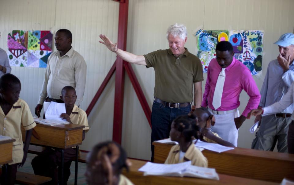 Former U.S. President and UN special envoy to Haiti Bill Clinton waves to the children of the Union Des Apotres – Prodev School in Cite Soleil, Port-au-Prince, Haiti, Monday Feb. 17, 2014. Clinton is in Haiti to visit several projects that focus on agriculture and the environment, including the Union Des Apotres – Prodev solar-powered school that his private foundation has assisted and a training school for Haitian coffee farmers. (AP Photo/Dieu Nalio Chery)