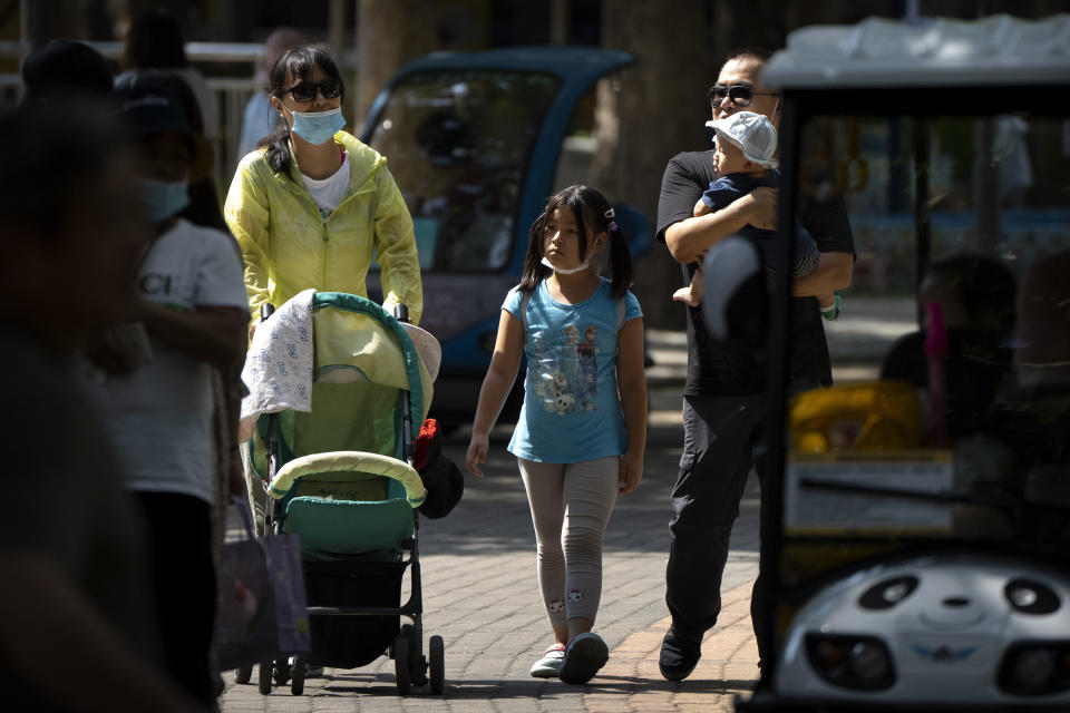 Adults and children walk along a path at a public park in Beijing, Saturday, Aug. 21, 2021. China will now allow couples to have a third child as the country seeks to hold off a demographic crisis that threatens its hopes of increased prosperity and global influence. (AP Photo/Mark Schiefelbein)