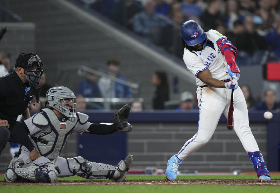 Toronto Blue Jays' Vladimir Guerrero Jr. (27) hits an RBI single as New York Yankees catcher Jose Trevino (39) looks on during the fourth inning of a baseball game in Toronto on Tuesday, April 16, 2024. (Nathan Denette/The Canadian Press via AP)