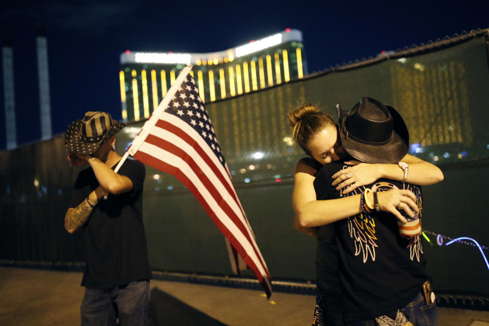 FILE - In this Oct. 1, 2018, file photo, Megan Murphy, right in hat, embraces Cara Knoedler as Kenneth Wright wipes his eyes on the first anniversary of the mass shooting in Las Vegas. Casino giant MGM Resorts International says more than 4,000 people are seeking compensation related to the Las Vegas Strip shooting that left 58 people dead, and it’s suing its insurance company for legal costs. A lawsuit filed Wednesday, June 19, 2019 in U.S. District Court in Las Vegas alleges breach-of-contract by Illinois-based Zurich American Insurance Co. (AP Photo/John Locher, File)