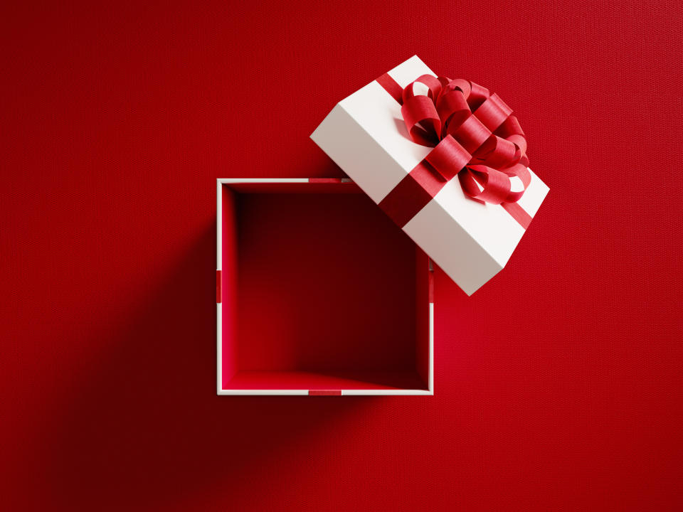 An open gift box with a ribbon on the lid, placed against a red background