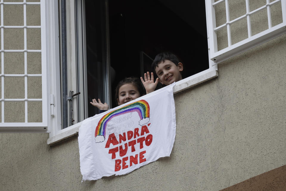 In this photo taken on Friday, March 13, 2020, Francesco and Greta Innominati wave after placing a banner reading "Everything is gone be all right" out of a window of their apartment in Rome. The nationwide lockdown to slow coronavirus is still early days for much of Italy, but Italians are already are showing signs of solidarity. This week, children’s drawings of rainbows are appearing all over social media as well as on balconies and windows in major cities ready, ‘’Andra’ tutto bene,’’ Italian for ‘’Everything will be alright.’’ For most people, the new coronavirus causes only mild or moderate symptoms. For some, it can cause more severe illness, especially in older adults and people with existing health problems. (AP Photo/Alessandra Tarantino)