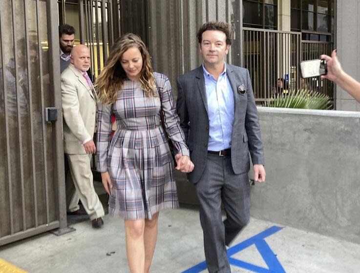 Danny Masterson wearing a suit is holding hands with Bijou Phillips who is wearing a plaid dress outside a courthouse