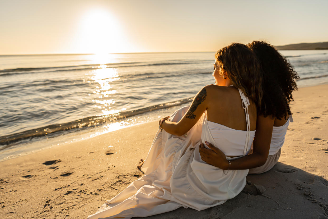 Two women embrace sat on a beach together