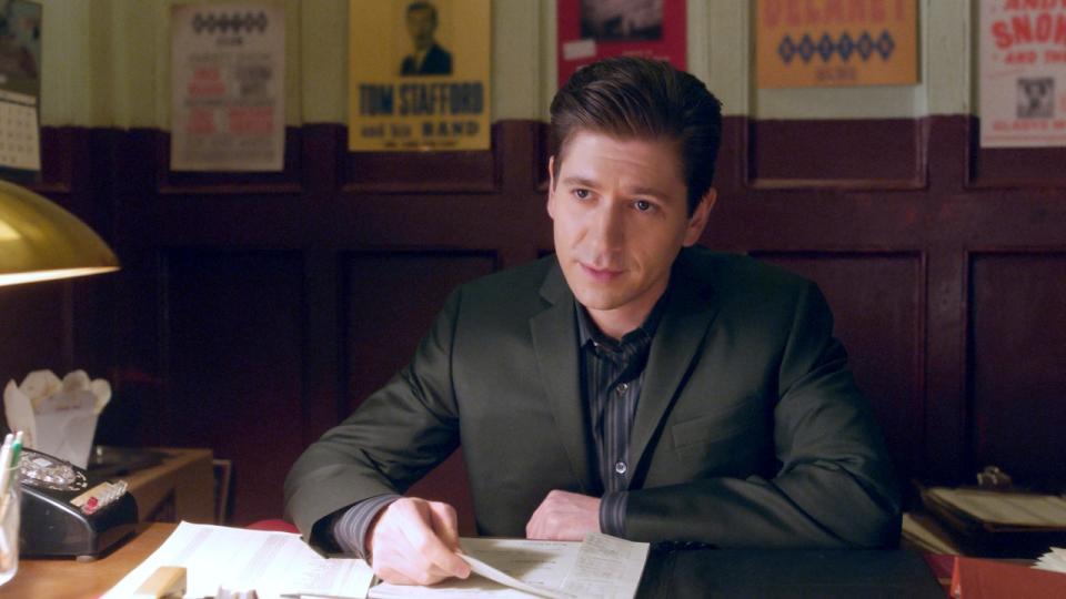 Michael Zegen sitting behind a desk as Joel