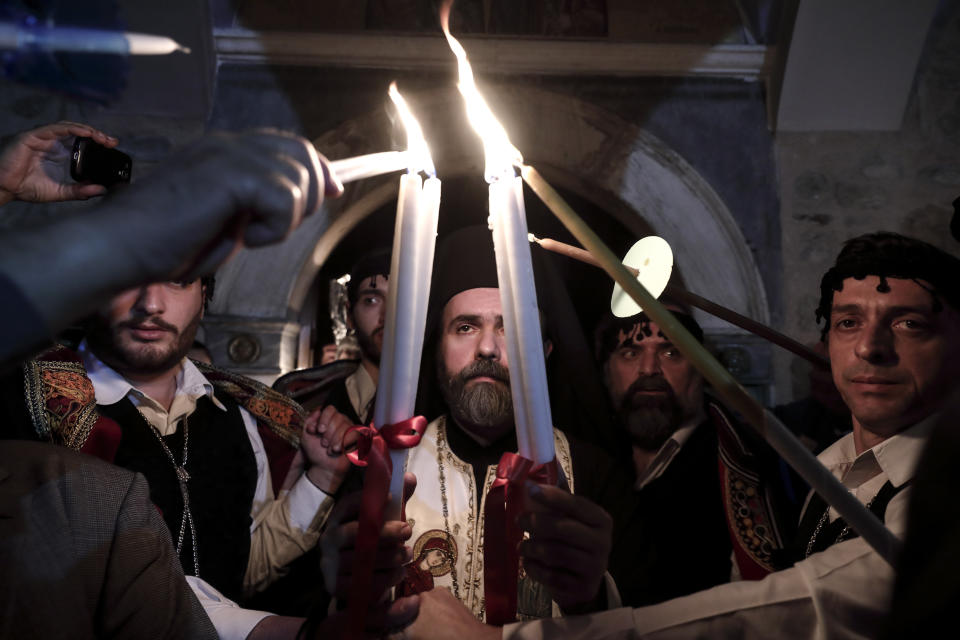 A Greek Orthodox priest lights candles of the faithful with Holy Fire brought from Jerusalem, at a church in Athens, on Saturday, April 27, 2019. A lantern carrying a flame lit in Jerusalem's Holy Sepulcher Church was welcomed in Greece with honors reserved for visiting heads of state. But a senior cleric boycotted the ceremony, miffed that the "Holy Flame" did not land within his see.(AP Photo/Yorgos Karahalis)