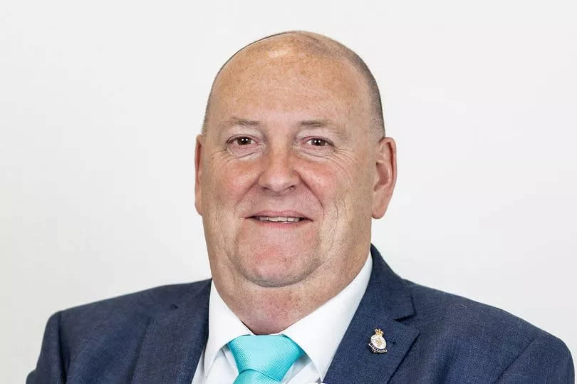 Man in his 60s in a suit with light-blue and white Reform UK political rosette