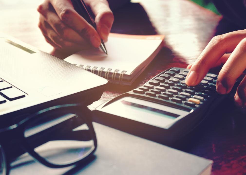 Close up of a person's hand using calculator and writing a note.