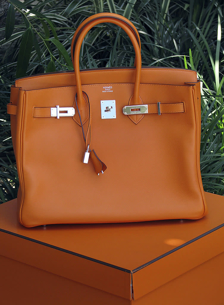 Orange luxury handbag on a matching box against a leafy background