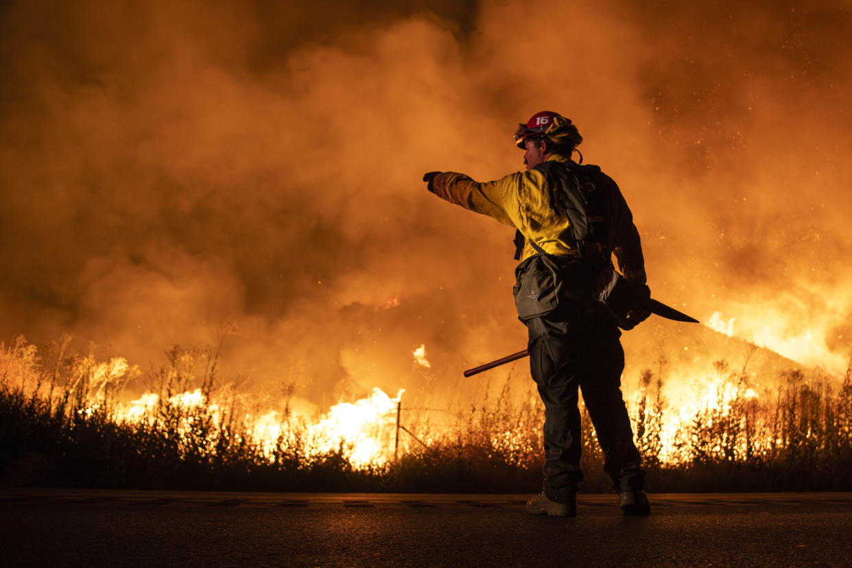 A firefighter, with his arm outstretched as he points toward the blaze, stands near an area engulfed by fire in Moreno Valley, Calif.