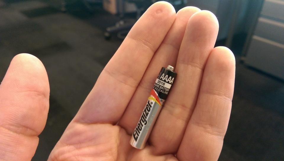 Person's hand holding a small AAAA Energizer battery to show its size compared to fingers