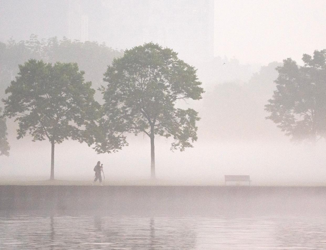 A photographer walks through the haze near Veterans Park as smoke from the Canadian wildfires continues to linger in the air in Milwaukee on Friday morning. The air is still unhealthy but it is improving in Milwaukee as the record-breaking haze caused largely by the fires begins to lift.