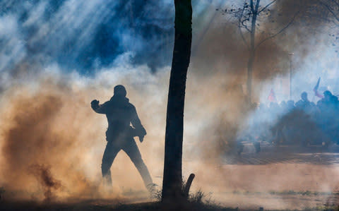 A protester is silhouetted in teargas during clashes with riot police - Credit: EPA