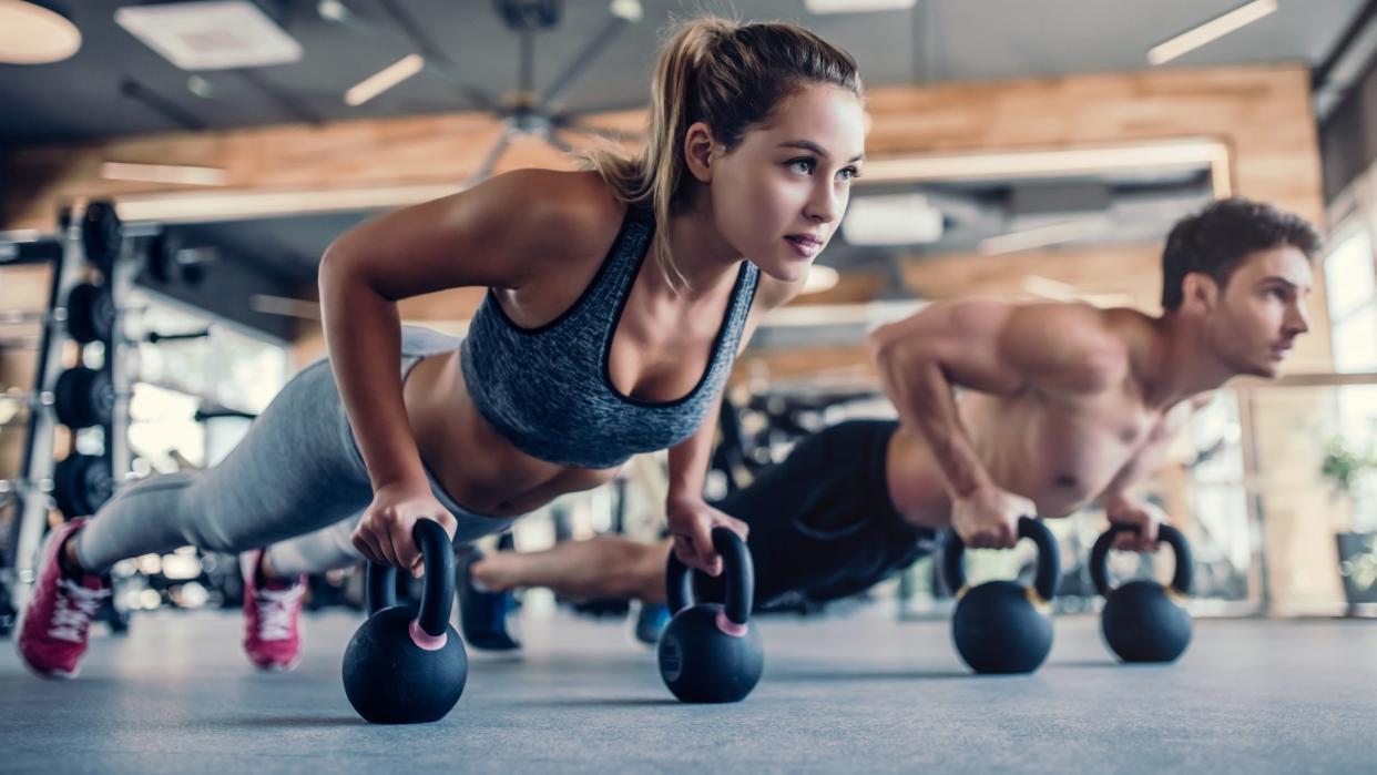  Man and woman in the gym performing a kettlebell plank holding two kettlebells in the plank position 