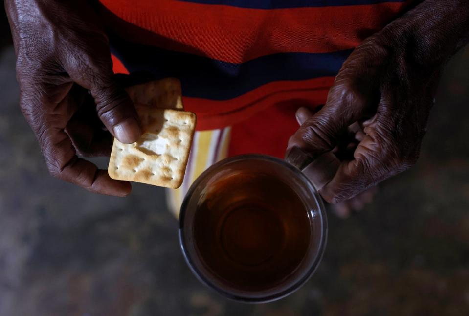 Susantha holds a cup of plain tea and two pieces of biscuit, the only food he has for the day (Reuters)