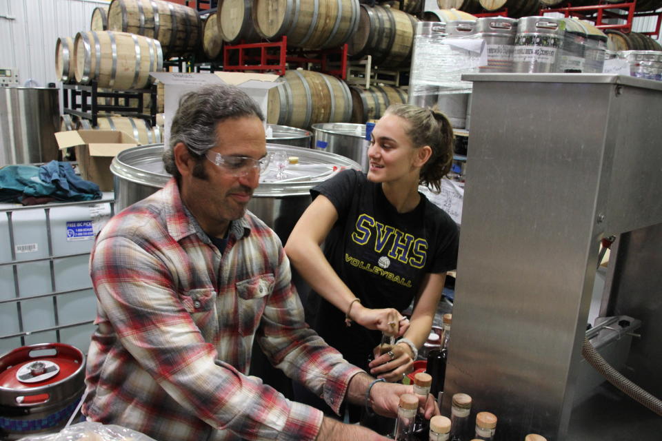 In this June 2, 2020, photo, Denali Brewing Co. founding partner Sassan Mossanen, left, and his daughter, Maya, cork bottles of coffee whiskey at Denali Brewing Co. in Talkeetna, Alaska. Talkeetna tourism businesses like the brewery and distillery, along with its main street brew pub, are feeling a financial squeeze after most major cruise ship companies have canceled their summer tourist seasons because of the coronavirus, meaning nearly half of Alaska's annual 2.2 million visitors won't be visiting Alaska. (AP Photo/Mark Thiessen)