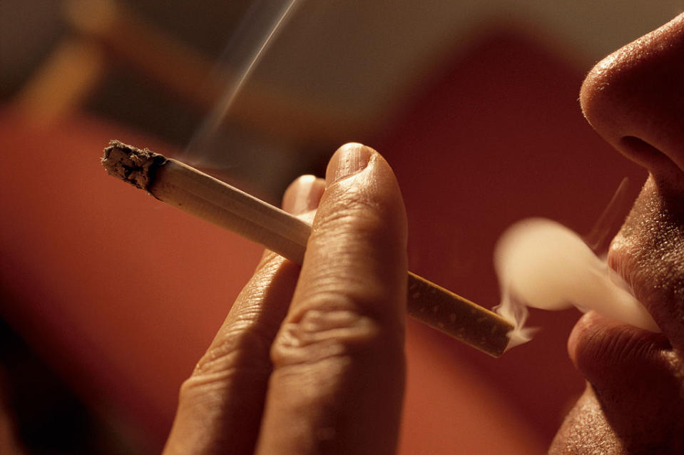 Close-up of a person smoking a cigarette, focusing on the hand and lips exhaling smoke